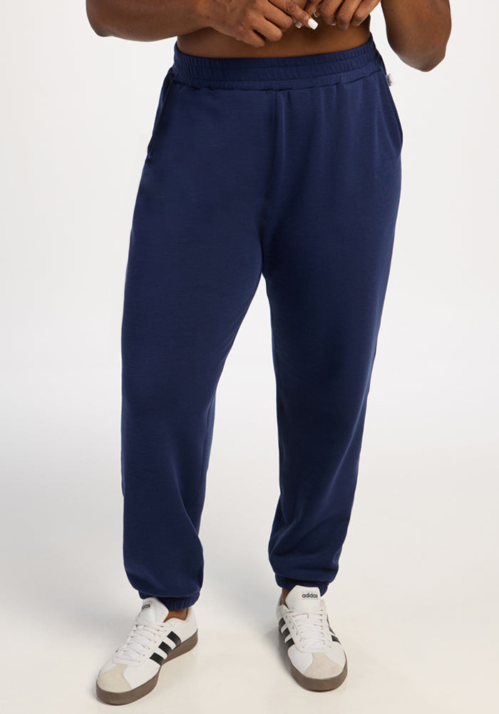Person in Woolx Parker Sweatpants - Ocean Cavern and white Adidas sneakers stands against a plain white background. 