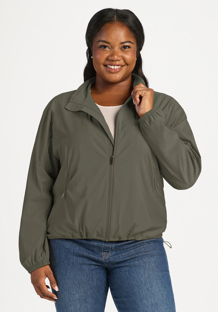A smiling woman wears a Sage Olive Cooper Windbreaker in olive green with a high collar and elasticized hem. 