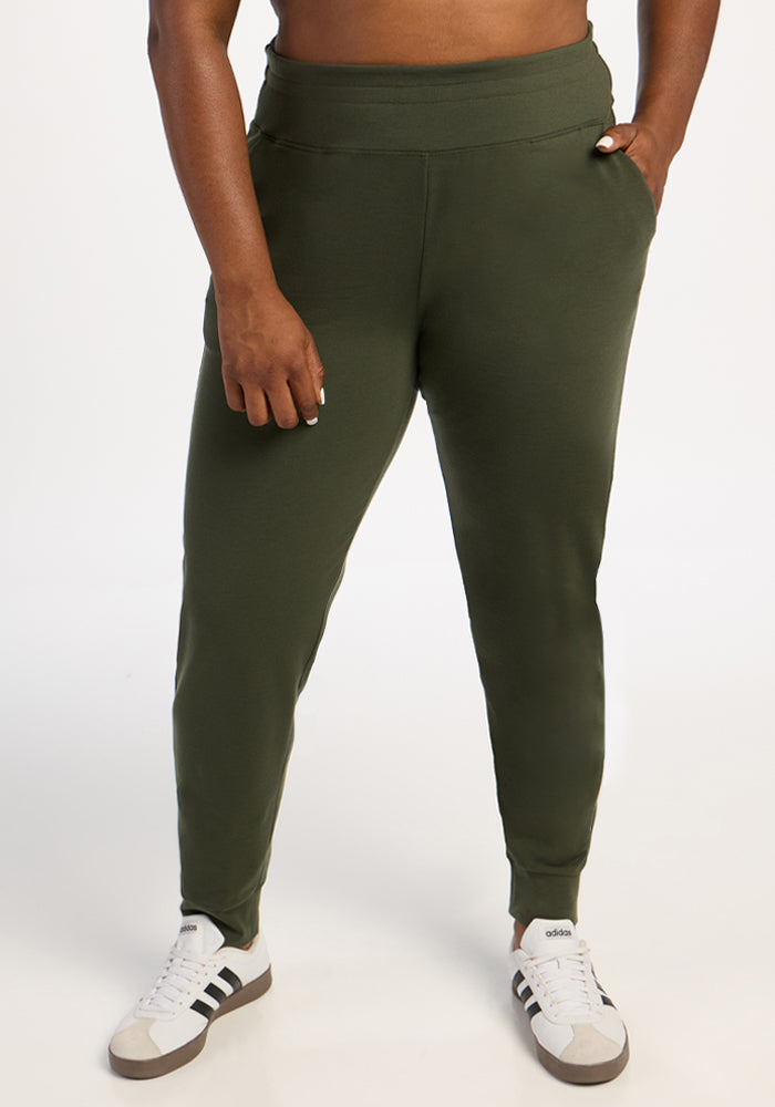Person in Woolx Madden Joggers (Everleaf) and white Adidas sneakers stands with one hand in pocket, white backdrop. 