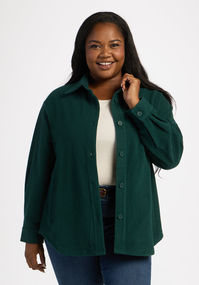 Woman smiles in Woolx Jovie Shacket - Deep Pine, layered over white top and blue jeans against a white background. 