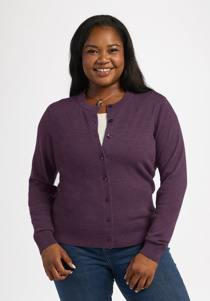 Smiling woman in the Woolx Caitlin Sweater - Purple Iris and blue jeans stands against a white background. 