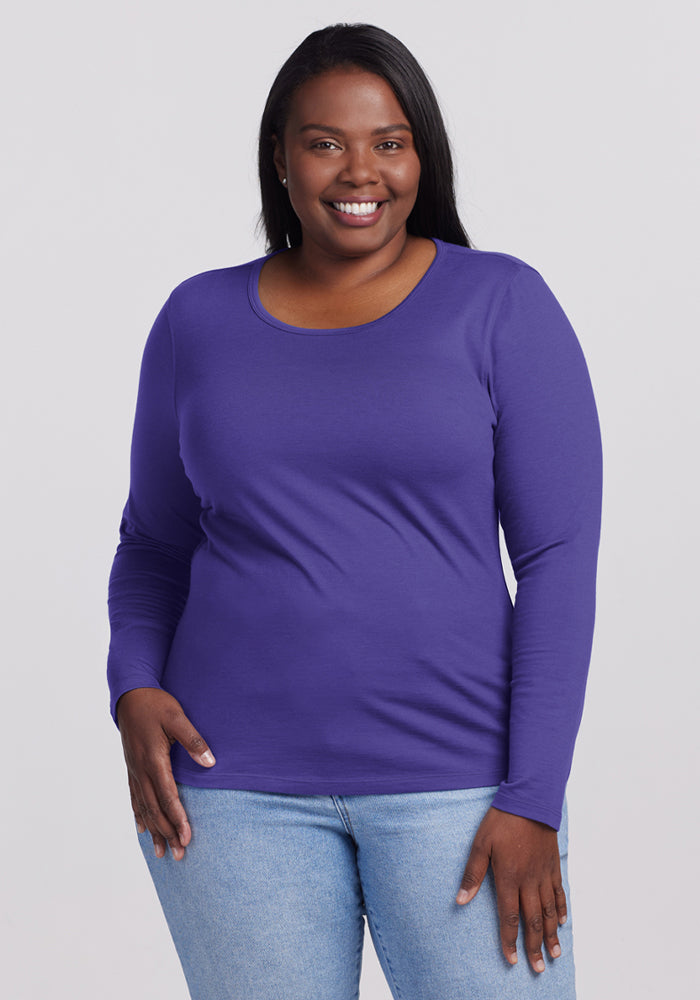 Woman in Woolx Remi Long Sleeve T-Shirt - Berry Indigo and light blue jeans stands against a plain light background. 