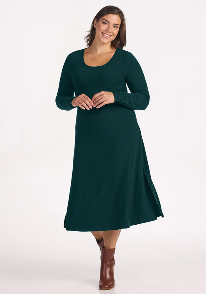 Smiling woman in the Woolx Caroline Ribbed Twirl Dress - Deep Pine and brown boots, on a white background. 
