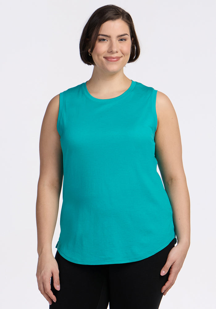 A woman with short brown hair wears the Woolx Bella Tunic Top in Cool Jade and black pants, standing and smiling against a plain white background. 