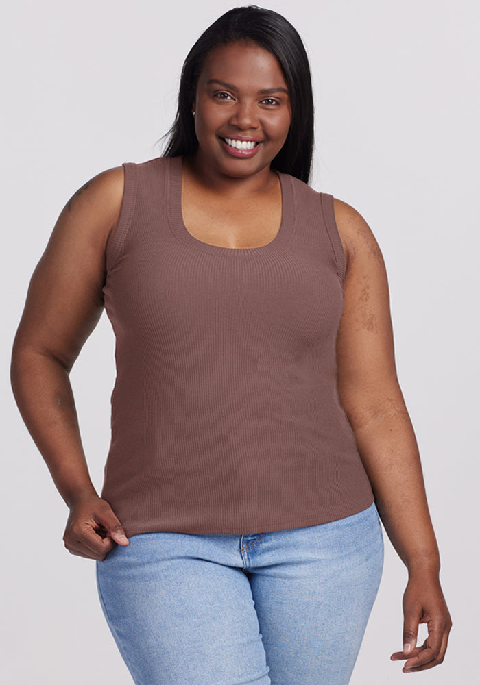 Smiling woman in a Woolx Sloane Ribbed Tank - Peppercorn and light blue jeans poses against a plain background. 