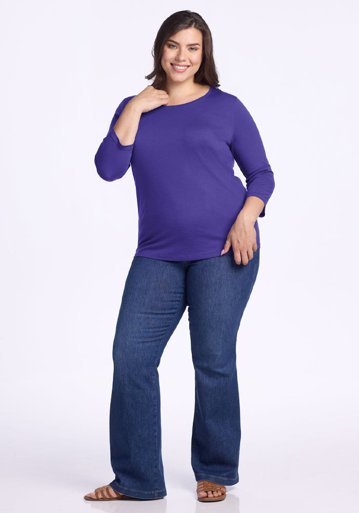 Woman smiling in a Woolx Jenny 3/4 Sleeve Crew Neck - Berry Indigo, blue jeans, and sandals against a white background.