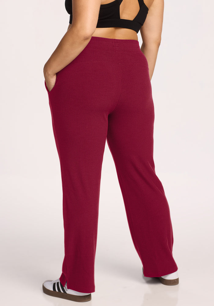Person in Woolx Luca Ribbed Pants - Beet Red, black top, sneakers, hands in pockets, shown from the back.