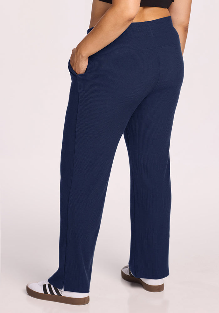 Model wears Woolx Luca Ribbed Pants - Ocean Cavern with white sneakers, hands in pockets, shown from the back.