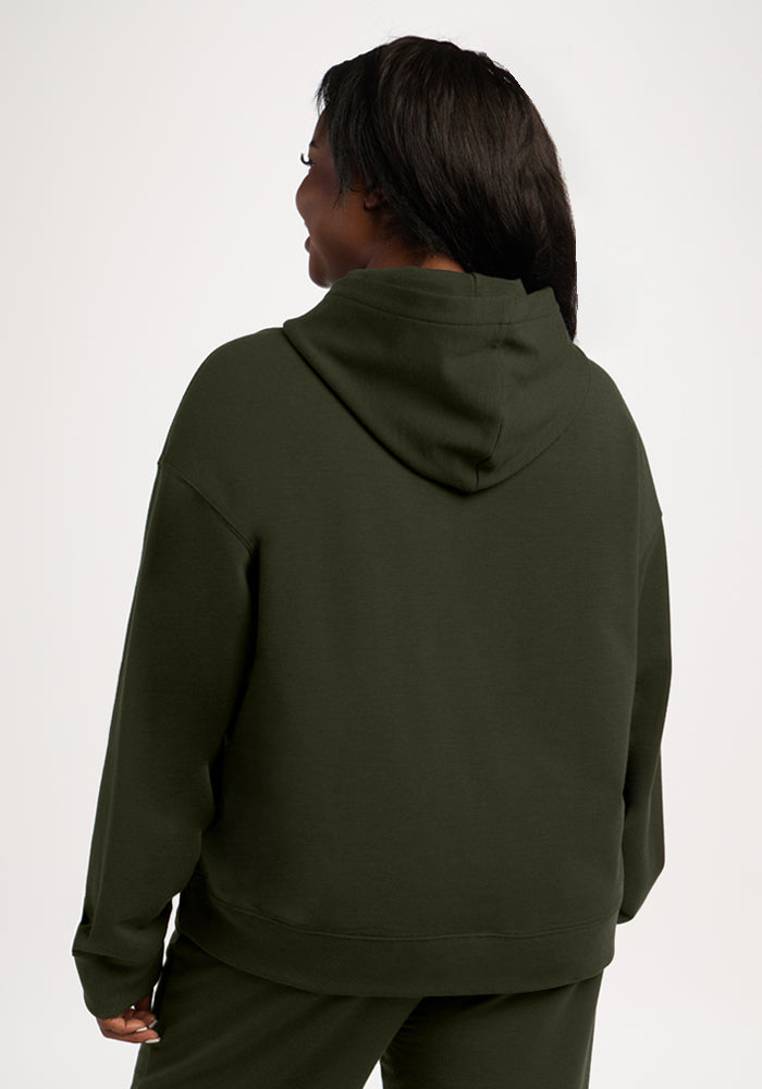 A person seen from the back wearing a dark olive green moisture-wicking merino wool Genevieve Hoodie - Duffel Bag.