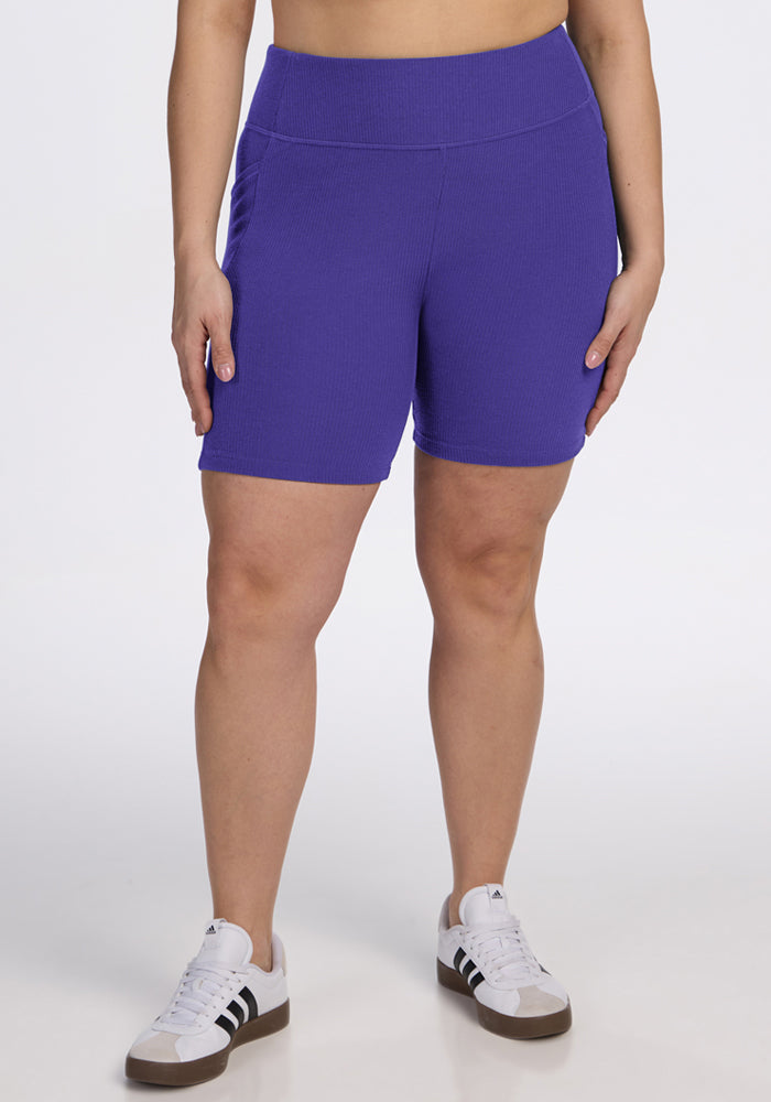 Person wearing Woolx Miley Bike Shorts - Berry Indigo and white sneakers, standing against a plain white background. 