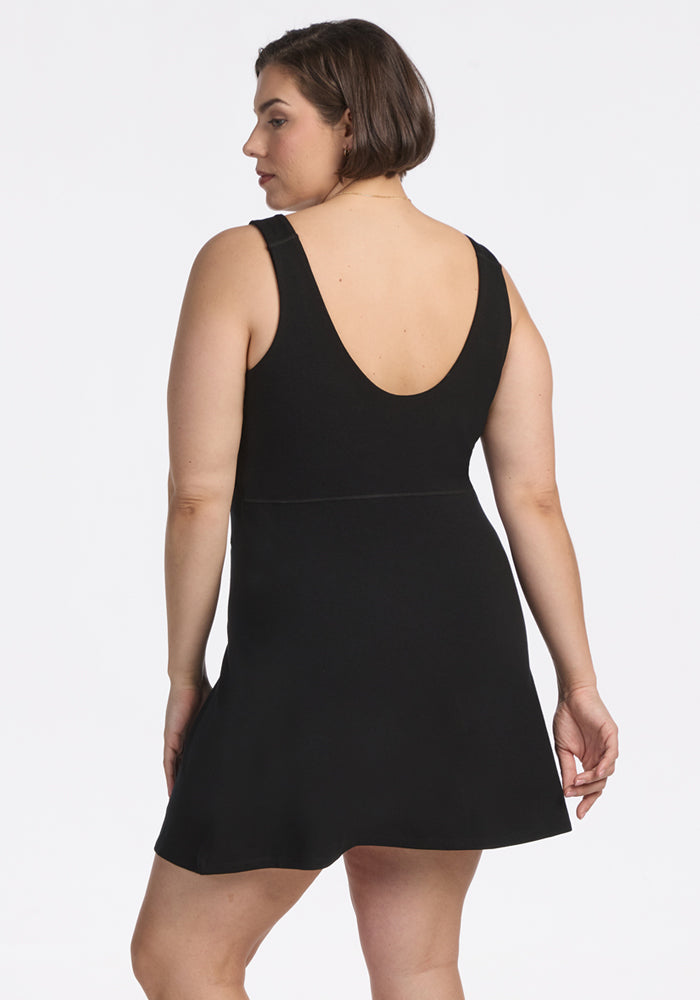 A person with short brown hair stands with their back to the camera in the Woolx Adrienne Active Dress - Black, a sleeveless, knee-length dress featuring a scoop back. The background is plain white.