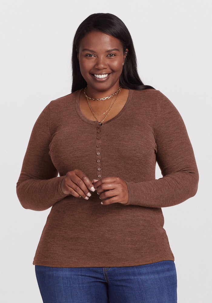 Smiling woman in a Woolx Reese Ribbed Henley - Sable Heather and blue jeans stands against a white background. 
