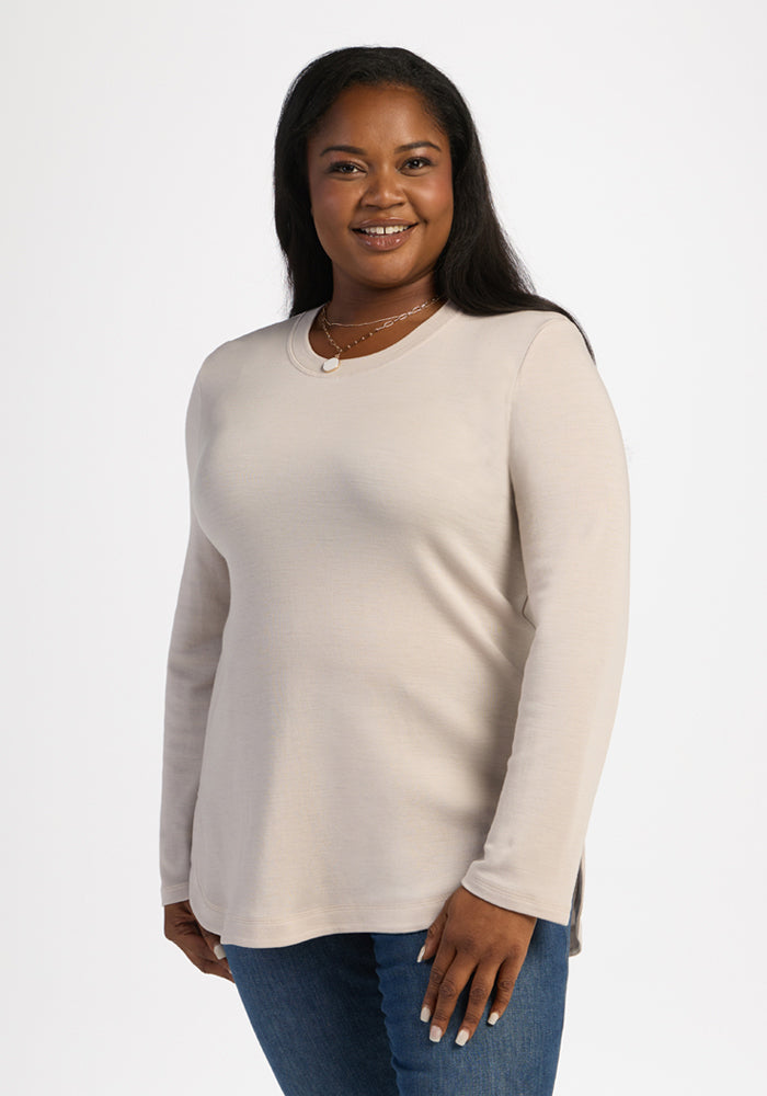 Woman in a Woolx Blair Tunic - Ecru and jeans, smiling with hands at her side, on a white background. 