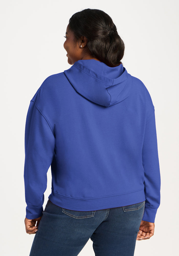 Woman standing back, wearing a Woolx Lizzy Hoodie in royal blue and jeans, her hair in a neat ponytail.