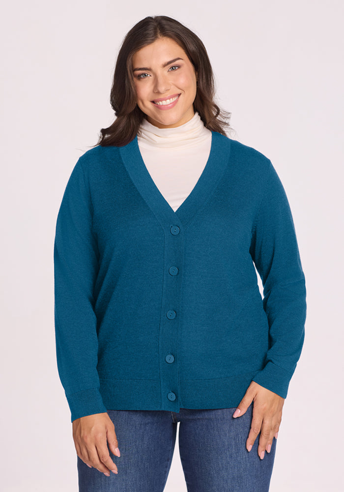 Woman in Woolx Gia Sweater - Blue Pine and white turtleneck, smiling against a plain light background. 