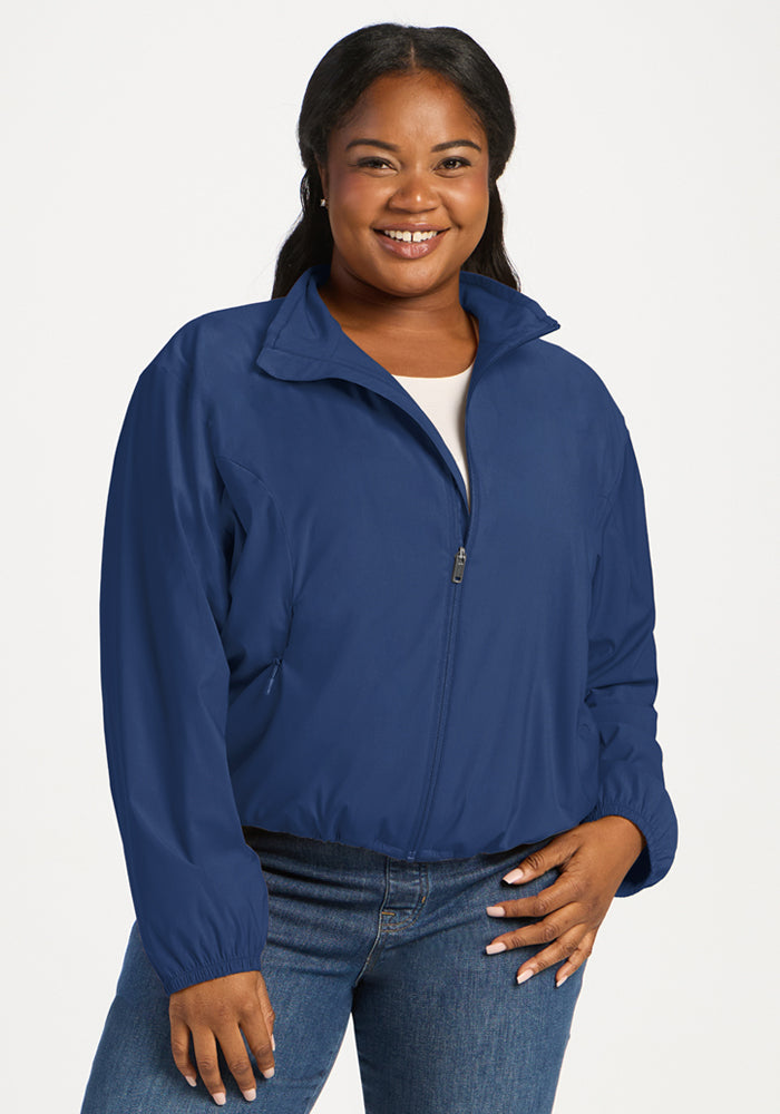 A woman wears a Vintage Indigo Cooper Windbreaker over a white shirt and jeans for a customizable fit. 