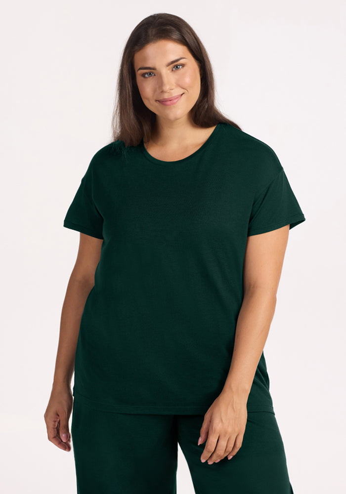 A smiling woman wearing a dark green Woolx Billie Lounge Tee - Deep Pine crewneck t-shirt. 