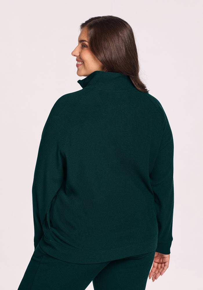 Woman smiles in Woolx Quinn Ribbed 1/4 Zip - Deep Pine, layered over pants with her head turned over her shoulder.