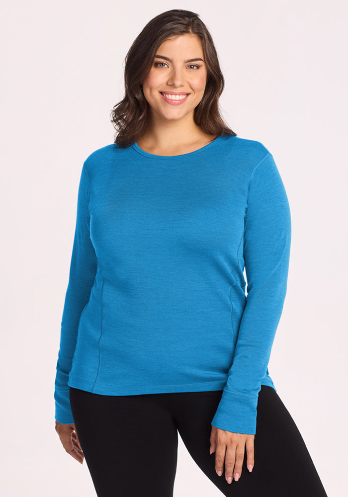 Woman in Woolx Hannah Long Sleeve Top - Blue Razz and black pants, smiling against a plain light background. 