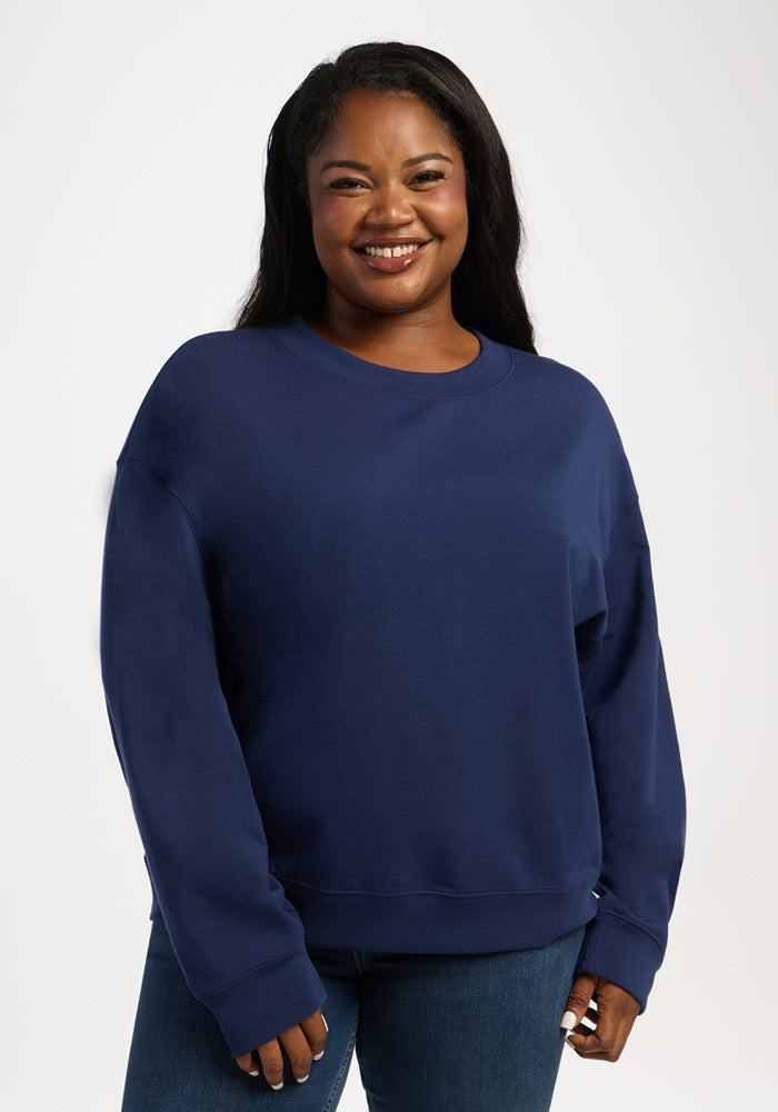A smiling woman wearing a dark blue merino wool Woolx Molly Crewneck - Ocean Cavern sweatshirt. 