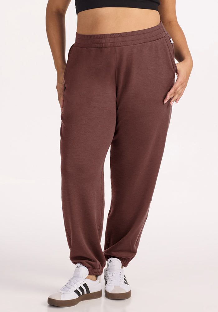 Person wearing Woolx Parker Sweatpants in Canyon Clay, white sneakers, and a black crop top, hands in pockets. 