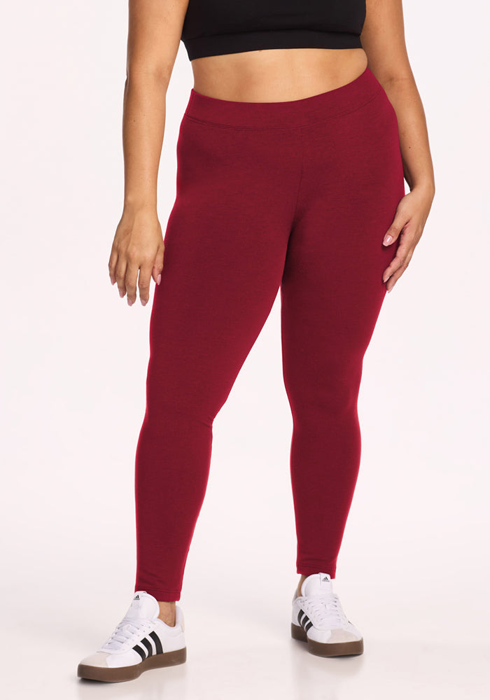 Model wears Woolx Stella Leggings - Pinot Noir, white sneakers, and a black crop top against a plain background. 