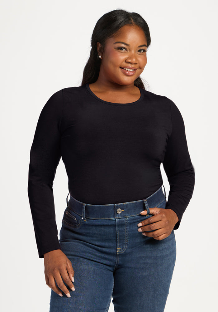 Woman smiling in Woolx Margot Bodysuit - Black and blue jeans, standing against a plain white background. 