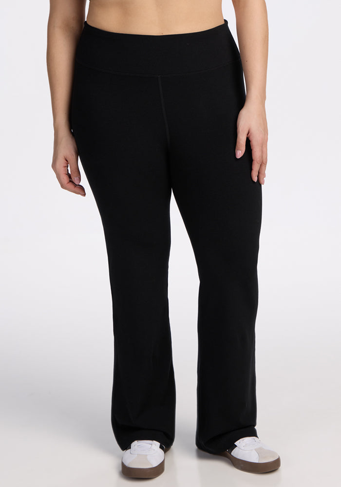 A person models the Woolx Morgan Flare Pants in black with white sneakers, standing against a plain white background. The image is cropped from mid-torso to feet. 