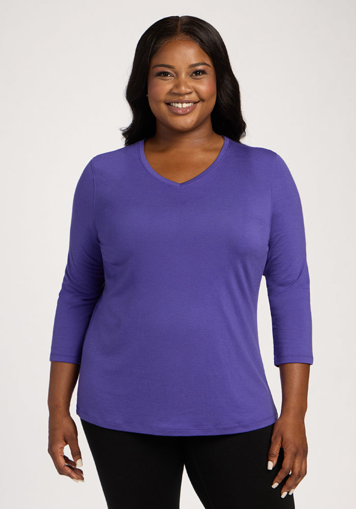 Smiling woman in a Woolx Elena 3/4 Sleeve V Neck - Berry Indigo and black pants, against a plain background. 