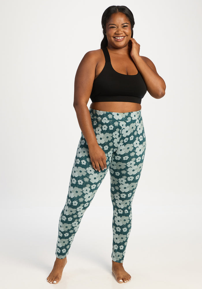 Smiling woman in Woolx Taylor Baselayer Leggings—Coastal Wildflower—stands barefoot against a plain white background.