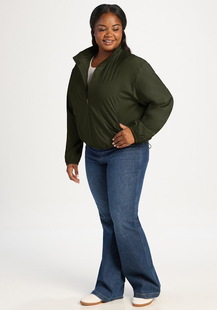 A woman wears a dark green Woolx Cooper Windbreaker - Duffel Bag and blue jeans made of all-season woven fabric.