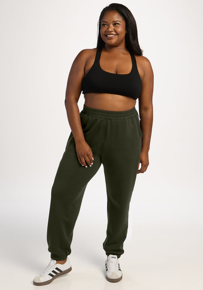 Smiling woman in a black sports bra and Woolx Parker Sweatpants - Duffel Bag stands against a plain background.
