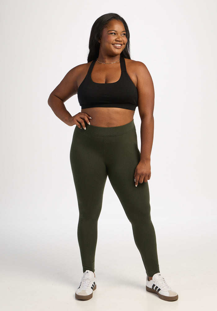 Woman smiles, facing right, wearing Stella Tall - Duffel Bag by Woolx, black sports bra, green leggings, white sneakers.