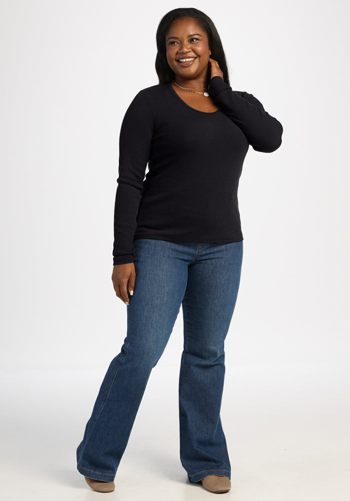 Woman smiles in Woolx Katie Ribbed Long Sleeve - Black, paired with blue jeans, hand gently touching her neck.