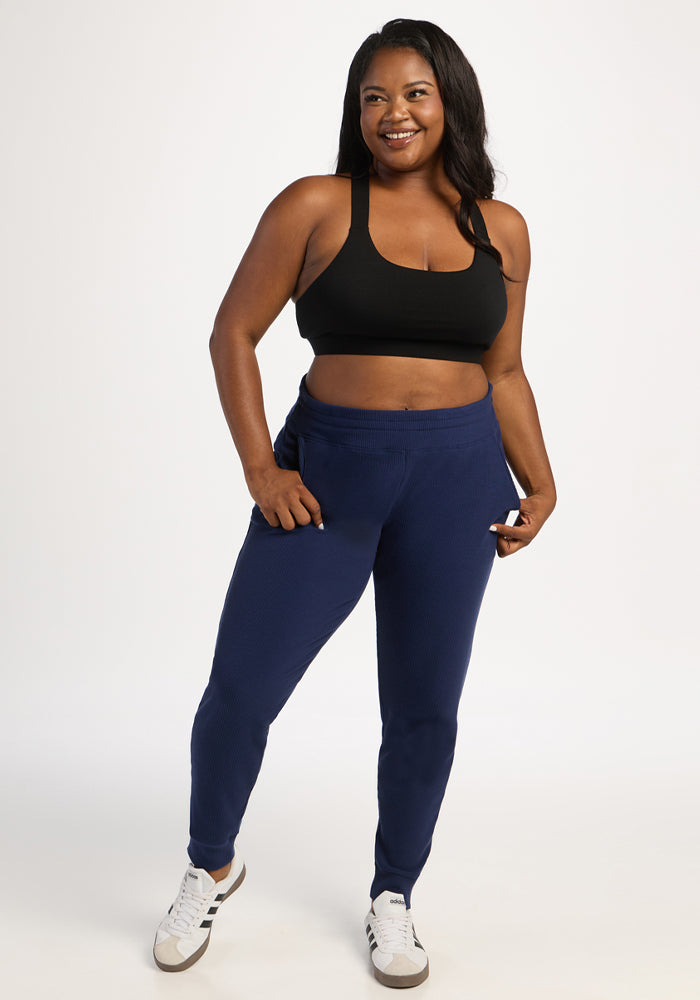 Woman in Woolx Lennon Ribbed Joggers - Ocean Cavern and black sports bra poses confidently against a white background.