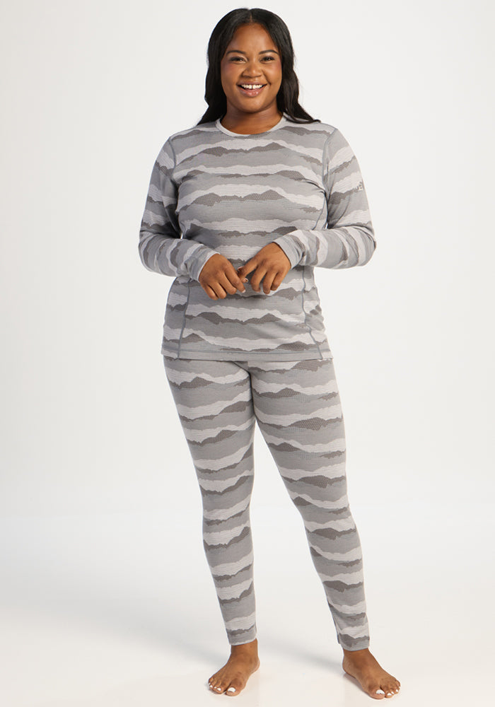 Woman smiling in a Woolx Maddie Baselayer Top - High Peaks, gray stripes, standing barefoot on white background.