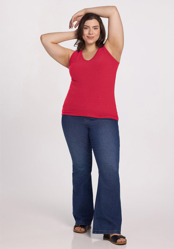 Smiling woman in Woolx Vivi Ribbed Tank - Berry Ice Pop and blue flared jeans, one arm raised above her head.