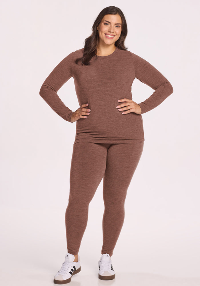 Woman smiles with hand on hip, wearing the Woolx Sadie Baselayer Top in Sable Heather, matching leggings, and sneakers.