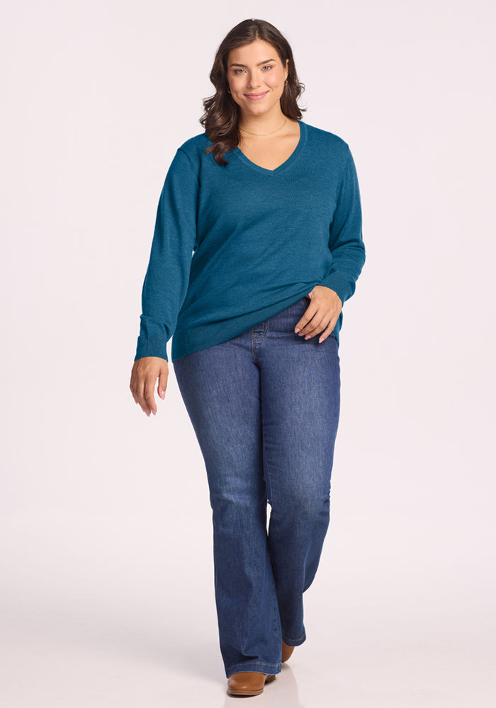 Woman in a Woolx Francesca Sweater - Blue Pine and blue jeans smiles, one hand in her pocket against a plain background.