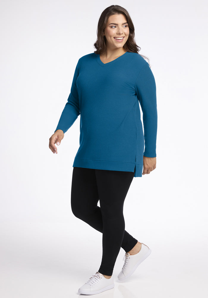 Woman in Woolx Evie Ribbed Tunic - Blue Pine, black leggings, and white sneakers walking and smiling on white.