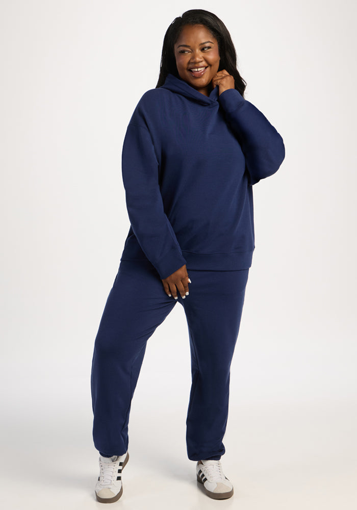 A woman wearing a navy blue Woolx Genevieve Hoodie - Ocean Cavern with matching sweatpants and white sneakers.