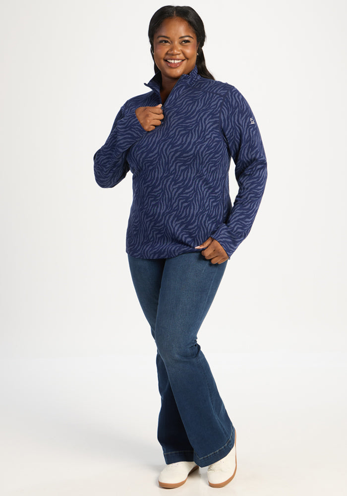 Woman wearing Woolx Emi 1/4 Zip in Midnight Safari and jeans poses against a white background, smiling.