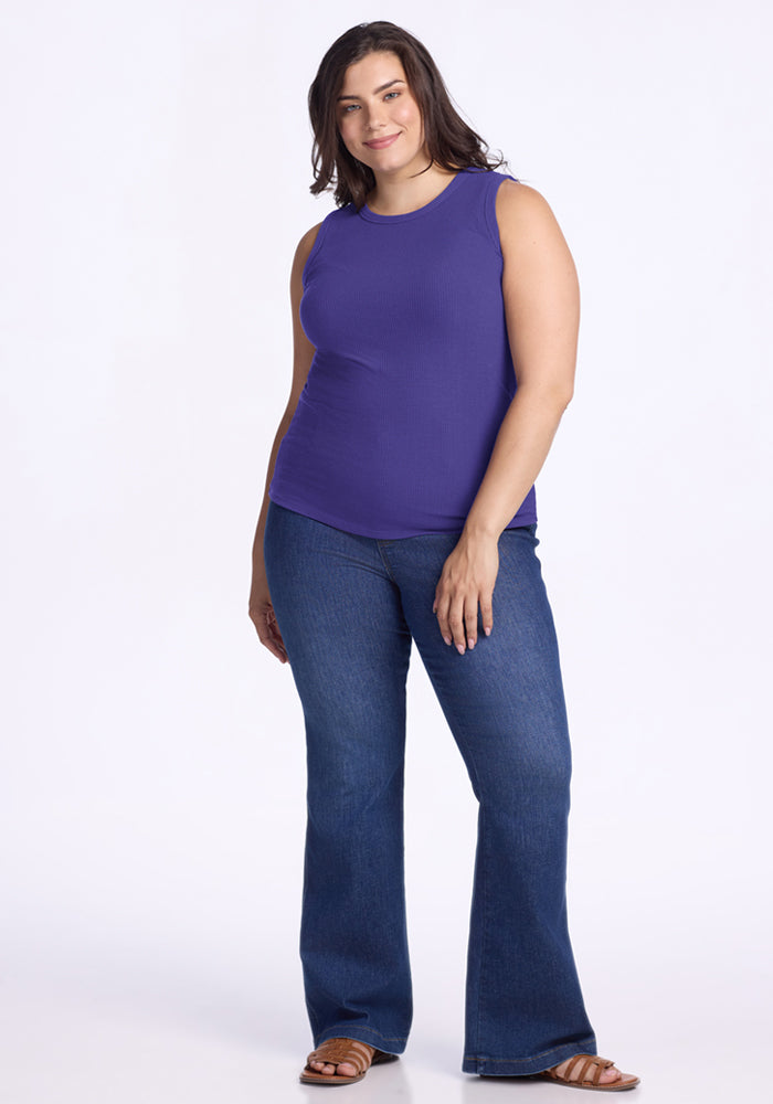 Woman in a Woolx Raegan Ribbed Tank Top - Berry Indigo, blue flared jeans, and sandals stands against a white background.