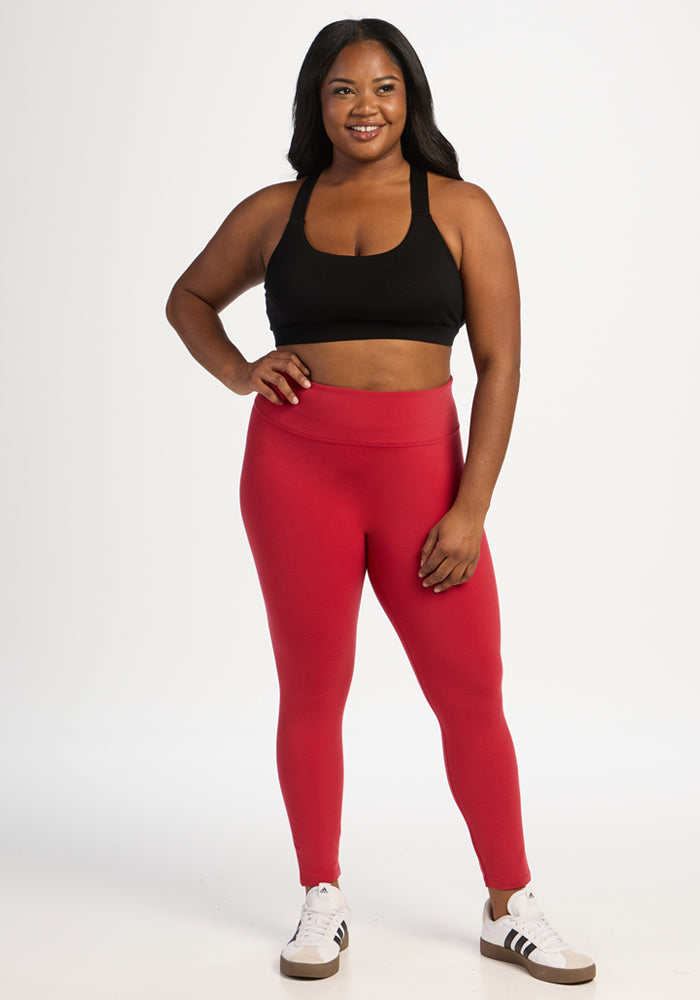 A person wearing a black sports bra, Angela Leggings - Maraschino Cherry, and white sneakers against a white background.