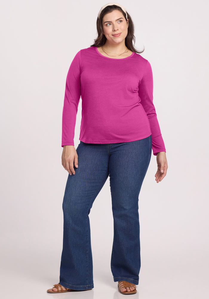 Smiling woman in a Woolx Remi Long Sleeve T-Shirt - Summer Sorbet, blue flared jeans, sandals, and a hair clip.