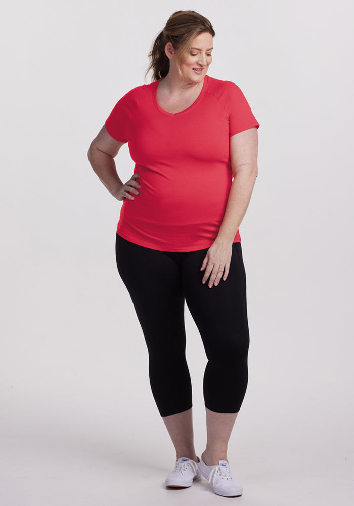 Woman wearing Woolx Mia V Neck – Berry Ice Pop, black leggings, and white sneakers, smiling against a plain background.