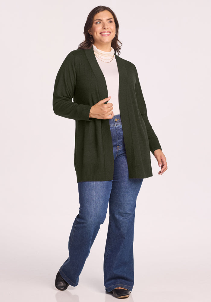 Woman in the Woolx Macie Sweater - Duffel Bag, white top, jeans, and black shoes stands smiling against a plain background.