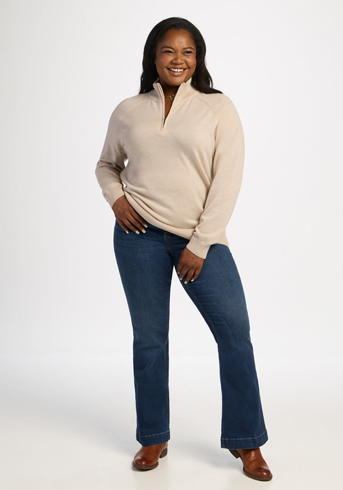 Woman wears Woolx Collins Half Zip Sweater in French Oak and blue jeans, smiling with hand on hip against white background.