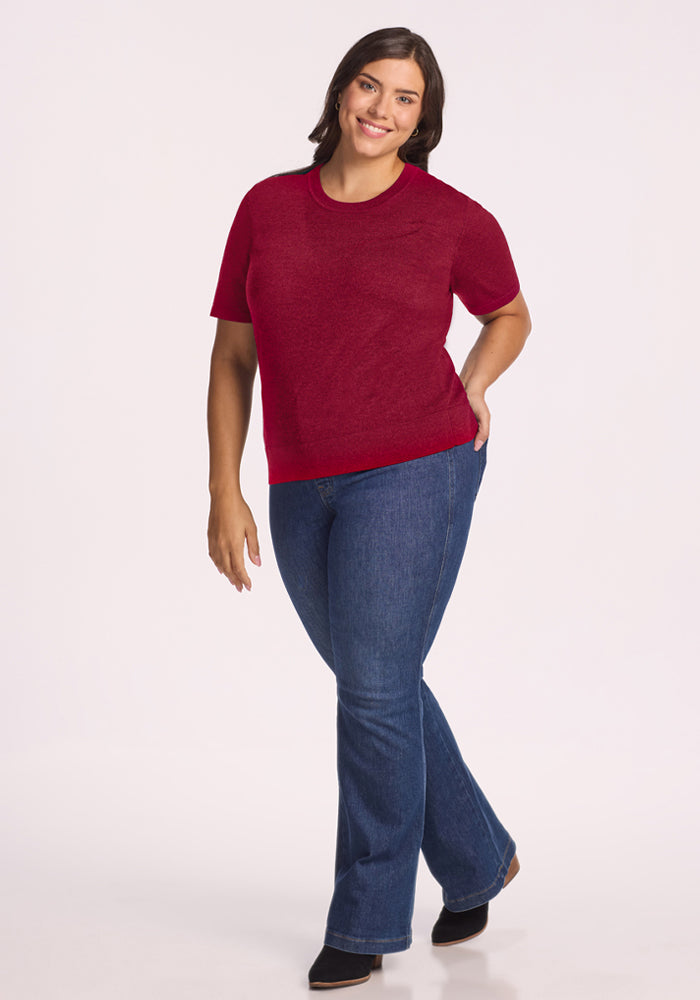 Woman wears the Woolx Anna Crew Sweater in Beet Red and blue jeans, smiling with one hand in her pocket.