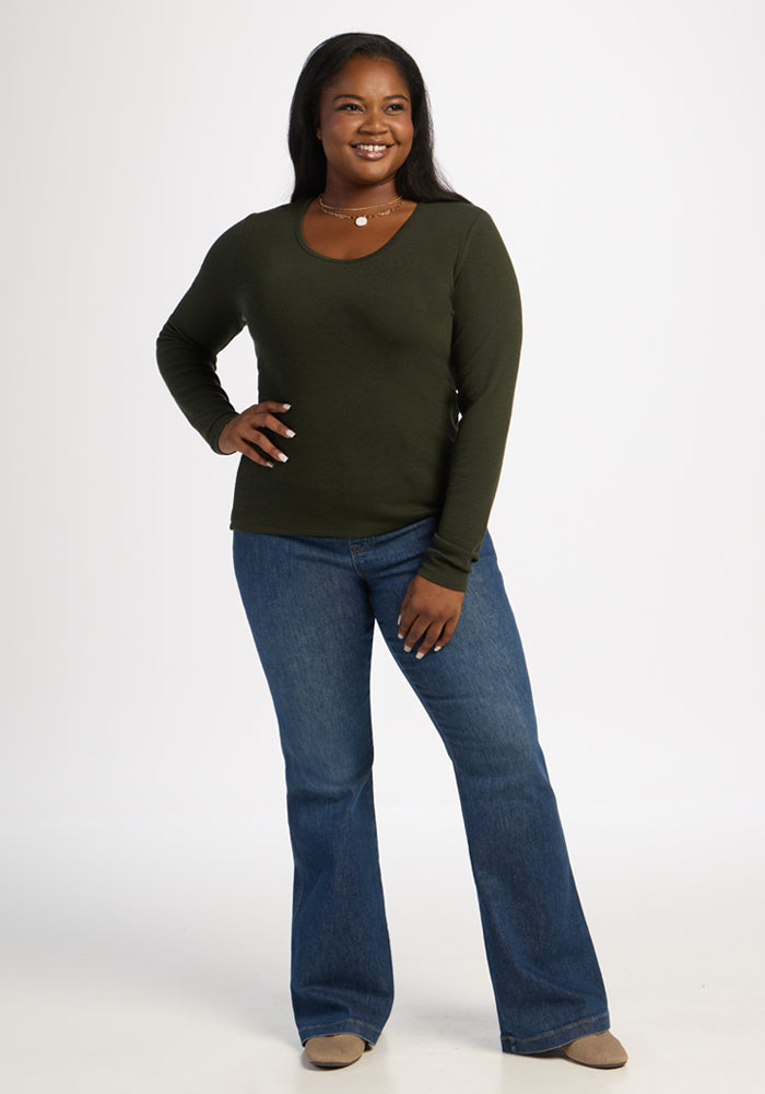 Woman wearing Woolx Katie Ribbed Long Sleeve in Duffel Bag and blue jeans smiles with hands on hips against white background.